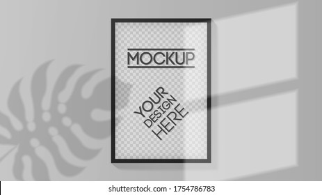 A black blank frame for a picture on the wall illuminated by sunlight from the window and tropical leave silhouette in empty gray room. Easy to place your design. Mockup Vector