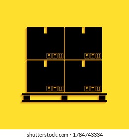 Black Cardboard boxes on pallet icon isolated on yellow background. Closed carton delivery packaging box with fragile signs. Long shadow style. Vector.