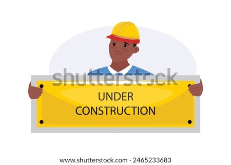 Black friendly man wearing a protective helmet and holding under construction banner in front of him
