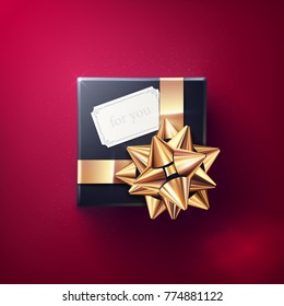 The black gift box with the white greeting card and glittering golden bow with ribbons isolated on red background. Vector realistic decoration element for holiday design. Top view