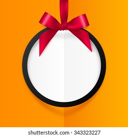 Black round frame hanging at red silky ribbon with bow at folded orange background