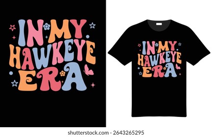 Maquete de camiseta preta com tipografia retro pastel colorido que lê In My Hawkeye Era com flores acompanhantes e ilustrações borboleta.