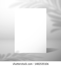 A  blank card or sheet of paper stands near a white wall with a shadow of a palm tree. Mockup for design