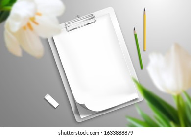 The blank notebook is clamped in the clipboard, two pencils and an eraser that are scattered over the surface. In the foreground are large tulip flowers. Top view mockup template