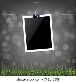 Blank photo frame in green grass field and light blurred bokeh background. Vector illustration.