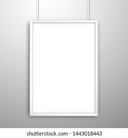 Blank white frame for a picture or poster hanging on strings near the wall. Mockup for design with shadow