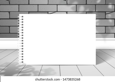 A blank white spiral notebook or album stands near the brick wall on the boards. The shadow of the Monstera plant is on top. Mockup for design