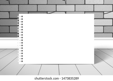 A blank white spiral notebook or album stands near the brick wall on the boards. Mockup for design with shadow