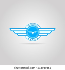 Blue vector sign of quadrocopter with wings. Blue circle vector sign with white silhouette quadrocopter with two wings and word Quadrocopter. Isolated illustration on gray background.