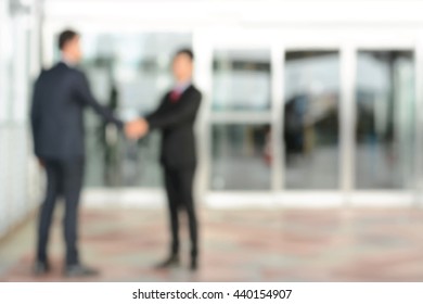 Blurred businessmen making handshake in front of office building doors - vector background