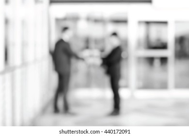 Blurred businessmen making handshake in front of office building doors in black and white - vector background