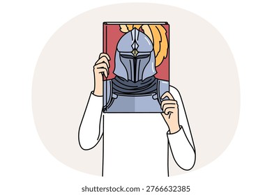 Book with knight on cover in hands of man covering face, reading literature about medieval soldiers. Man pretends to be knight in armor, dreaming of participating in gladiatorial tournaments.