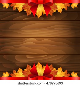 Border of autumn maples leaves decorated with a red bow on a wooden background.