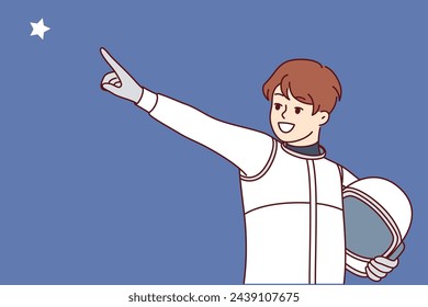 Boy astronaut points finger at star and holds spacesuit in hands for flight into space, dreaming of becoming member of spaceship crew. Child astronaut dreams of being like cosmonauts flying into orbit