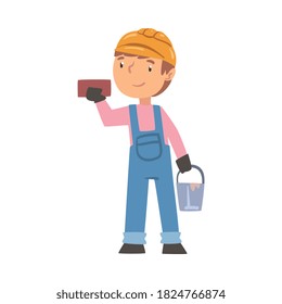 Boy Construction Worker with Bucket and Brick, Cute Little Builder Character Wearing Blue Overalls and Hard Hat with Professional Tools Cartoon Style Vector Illustration