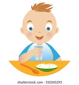 Boy having breakfast , holding a glass of milk and a plate of porridge and a spoon on the table