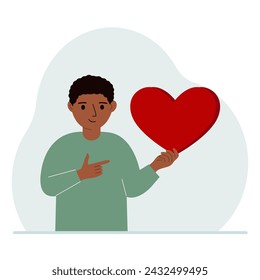 A boy holds a big red heart in his hand. The concept of volunteering, romantic relationship or love.