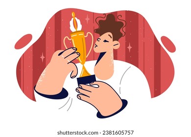 Boy kisses golden cup after winning competition or sports tournament among elementary school students. Teenager guy celebrating academic achievements holding olympiad winner cup in hands