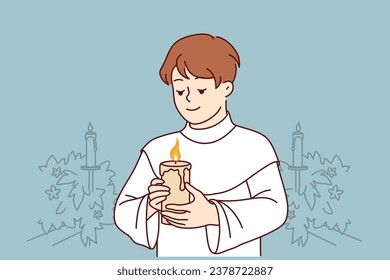 Boy participates in holy communion and holds burning candle for christian religious ritual in church. Child in clothes for communion ceremony in church smiles, wanting to become true believer catholic