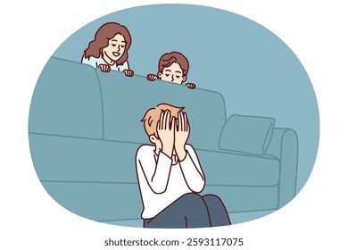 Boy plays hide and seek with friends sitting near sofa and waiting for other children to hide. Three cheerful children spend time together and enjoy weekend or summer school holidays