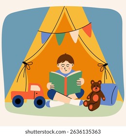Garoto lendo o livro dentro da barraca de brincar com brinquedos. Menino sentado em uma barraca de jogos interior acolhedora lendo um livro, cercado por um ursinho de pelúcia, caminhão de brinquedo e almofada.  