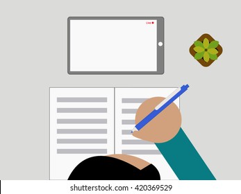 A boy is watching online tutorial and taking notes with a bird eyes view.