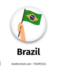 Brazil flag in hand, round icon with shadow isolated on white. Human hand holding flag, vector illustration