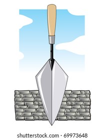 Brick layers trowel in front of a grey brick wall and blue sky