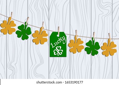 Bright Congratulations on St. Patrick's Day with good luck. Vector flat illustration with green and yellow clover leaves and a stick of “Luck” on clothespins On the light wooden table background.