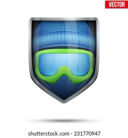 Bright metallic shield in the winter cap and ski goggles inside. Editable Vector Illustration isolated on white background.