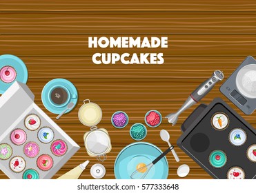 Brown wooden kitchen desk with blue ceramic crockery, kitchen devices, ingredients and coloured cupcakes in the box. Top view.