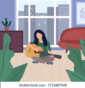 Brunette woman sitting in lotus position on the floor and playing the guitar. Girl playing an acoustic guitar.  Covid-19 quarantine-stay home concept. Girl on a background of a window at home. 