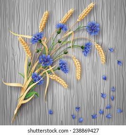 Bunch of wheat ears and blue cornflowers with scattered petals on grey  wood background.