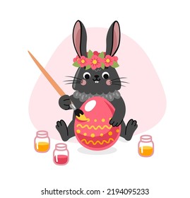Bunny coloring an easter egg. Cute black rabbit in flower wreath. Cartoon character. Vector flat illsutration.