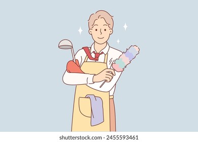 Business man in housewife apron is doing housework and cleaning or cooking after returning from work. Guy in formal clothes holds scrubber and brush for housework, while wife is away from home.