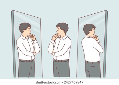 Business man looks in mirror trying on new formal clothes and touches chin with smile. Guy tries on business shirt and trousers for going to work and corporate meetings with manager.