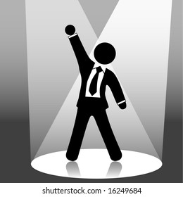 A Business Man Symbol Raises His Fist In Celebration Of Success On Stage In A Spotlight.