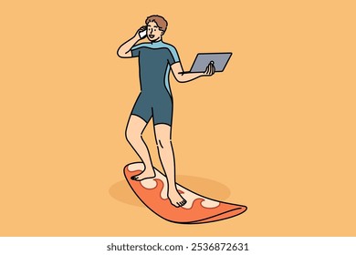 Hombre de negocios trabaja de pie en tabla de surf, con la computadora portátil y el teléfono móvil en las manos. Chico feliz en traje de buceo utiliza tabla de surf y gadgets independientes al mismo tiempo, trabajando mientras está de vacaciones.