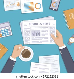 Business news. Businessman holding a newspaper and coffee cup on the desktop. Coffee break, breakfast, lunch, documents, purse, calculator, notebook, wrist watch. View from above