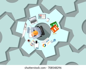 Business process or management concept design. Technology businessman with gadgets sitting at desk shaped as cogwheel brainstorming a project 