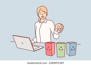 Business woman separates trash for recycling, sitting at table with laptop and miniature trash cans. Happy girl takes care of nature by properly sorting garbage and not mixing organic waste with paper