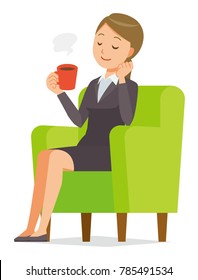 A business woman in a suit sits on a sofa and is drinking coffee