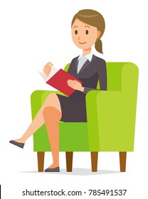 A business woman in a suit sits on a sofa and is reading books