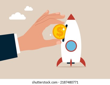 Businessman hand investor put money coin into innovative rocket to launch company. Funding startup company or venture capital investment.