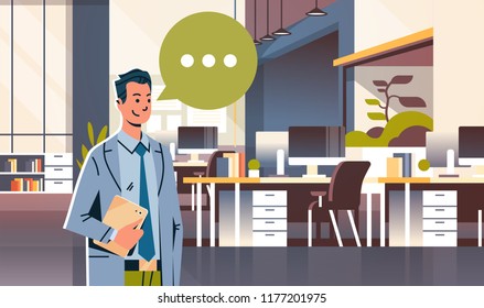 businessman holding tablet speech chat bubble icon over modern workplace cabinet room office interior business man cartoon character portrait flat horizontal vector illustration