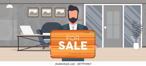 A businessman is holding a wooden sign with the inscription for sale. Young man in business suit holding a wooden sign. The concept of selling an apartment, office or building. 
