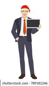 Businessman in Santa hat  with hand in pocket showing blank digital tablet PC. Full length portrait of businessman in a flat style. Vector illustration.