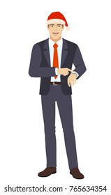 Businessman in Santa hat pointing at his watch. Full length portrait of businessman in a flat style. Vector illustration.