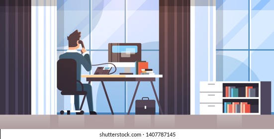 businessman sitting at workplace desk rear view business man using computer while talking on landline phone working process concept creative office interior flat horizontal