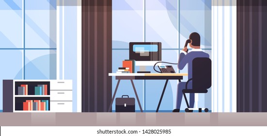 businessman sitting at workplace desk rear view business man using computer while talking on landline phone working process concept creative office interior flat horizontal